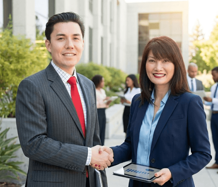 Two business people shaking hands in front of a building.